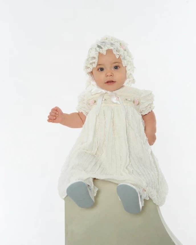 A baby in a lace dress and bonnet, sitting on a column