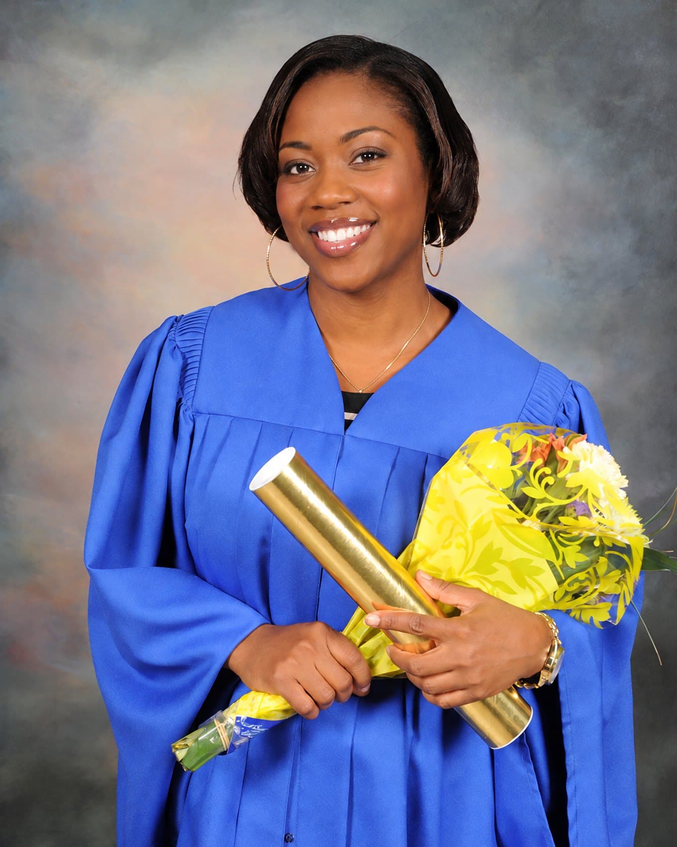 A graduate in a blue gown, with her diploma and flowers